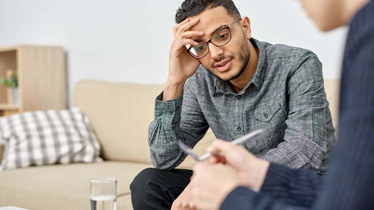 Close-up shot of young psychologist taking notes on clipboard while consulting depressed mixed-race patient during therapy session at cozy office