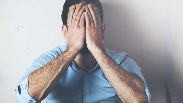 depressed man covering his face with both of his hands