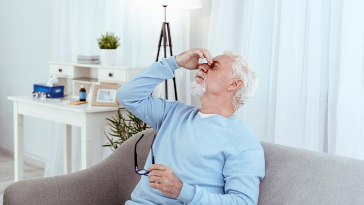 Low blood pressure. Tired senior man touching nose bridge and holding glasses