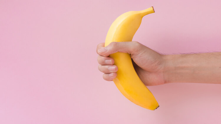 Male hand holding a banana isolated on pink background.