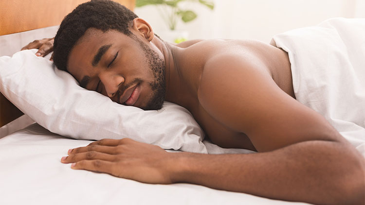 Naked black man sleeping in bed at home