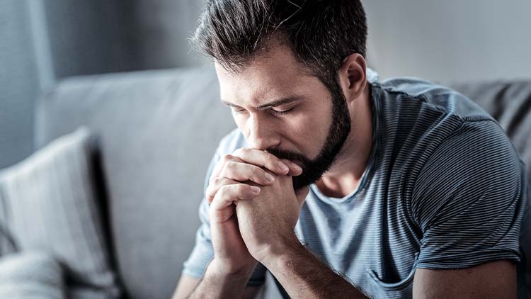 Serious cheerless unhappy man holding his chin and looking down while thinking what to do about his problem