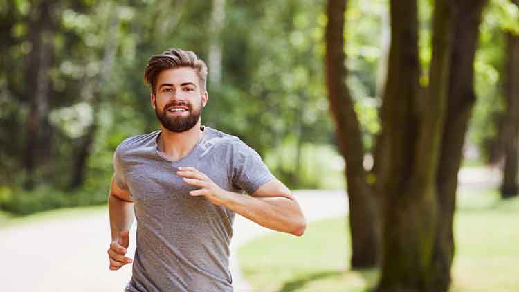 Smiling young man running in the park during summer