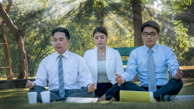 Office workers sat in the park meditating on sunny day