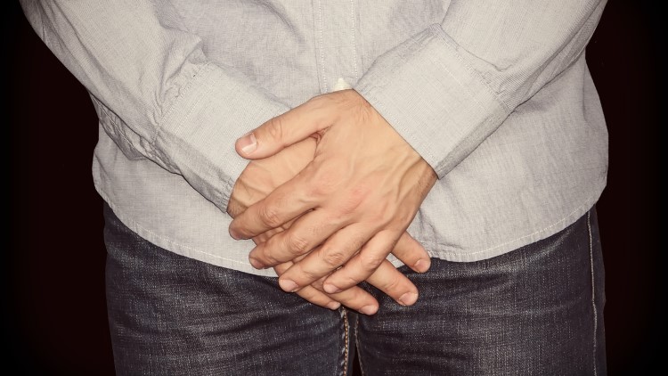 Clothed man's hands covering groin area