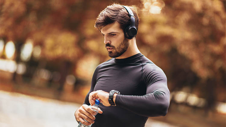 Portrait of young man on a morning jogging in the autumn park, man listening to music with headphones