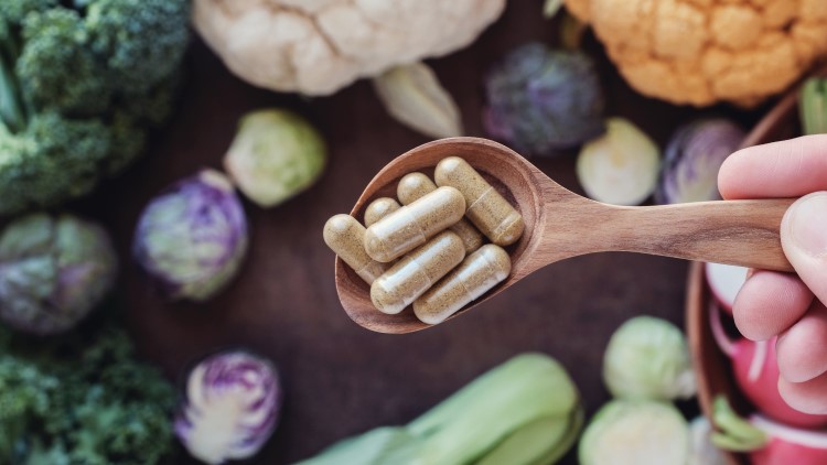 Pills on wooden spoon surrounded by vegetables