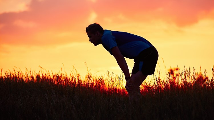 Man catching breath after running through grass at sunset