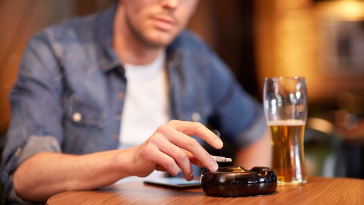 Man drinking and smoking cigarette at table in bar