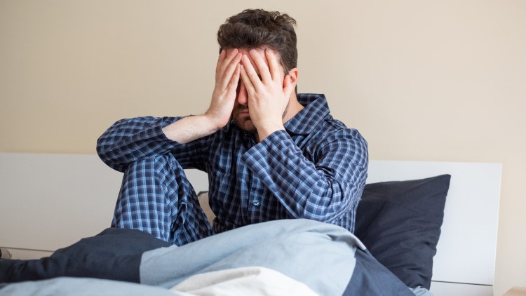 Man sat in bed with hands over face feeling bad