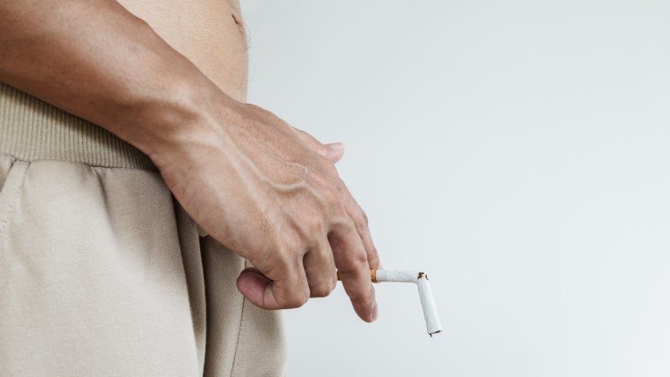 Man holding a snapped cigarette near groin