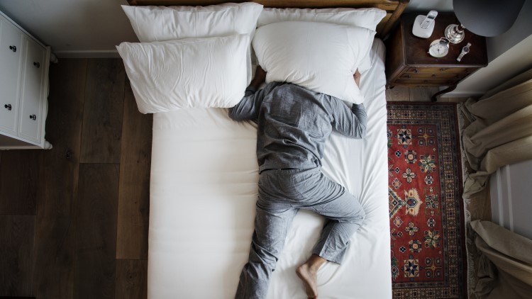 Man drowning out noise pollution holding pillow over his head in bed