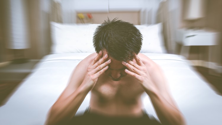 Man sat at end of bed holding head blurred background