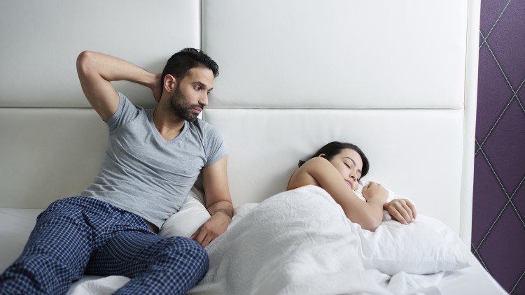 Man sat up in bed looking at partner asleep