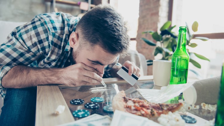 Man snorting drugs with pizza, alcohol and casino chips on table