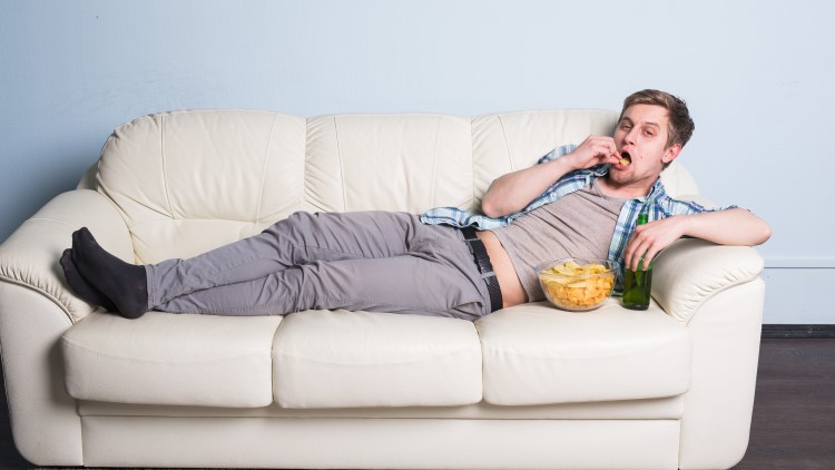 Man with beer and chips watching TV on sofa