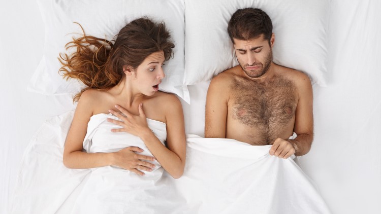 Woman looking shocked at man's penis under bedsheets