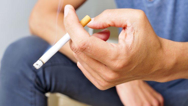 Young man sat down with lit cigarette in hand