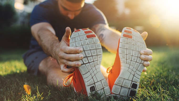 Young man sat in park stretching legs